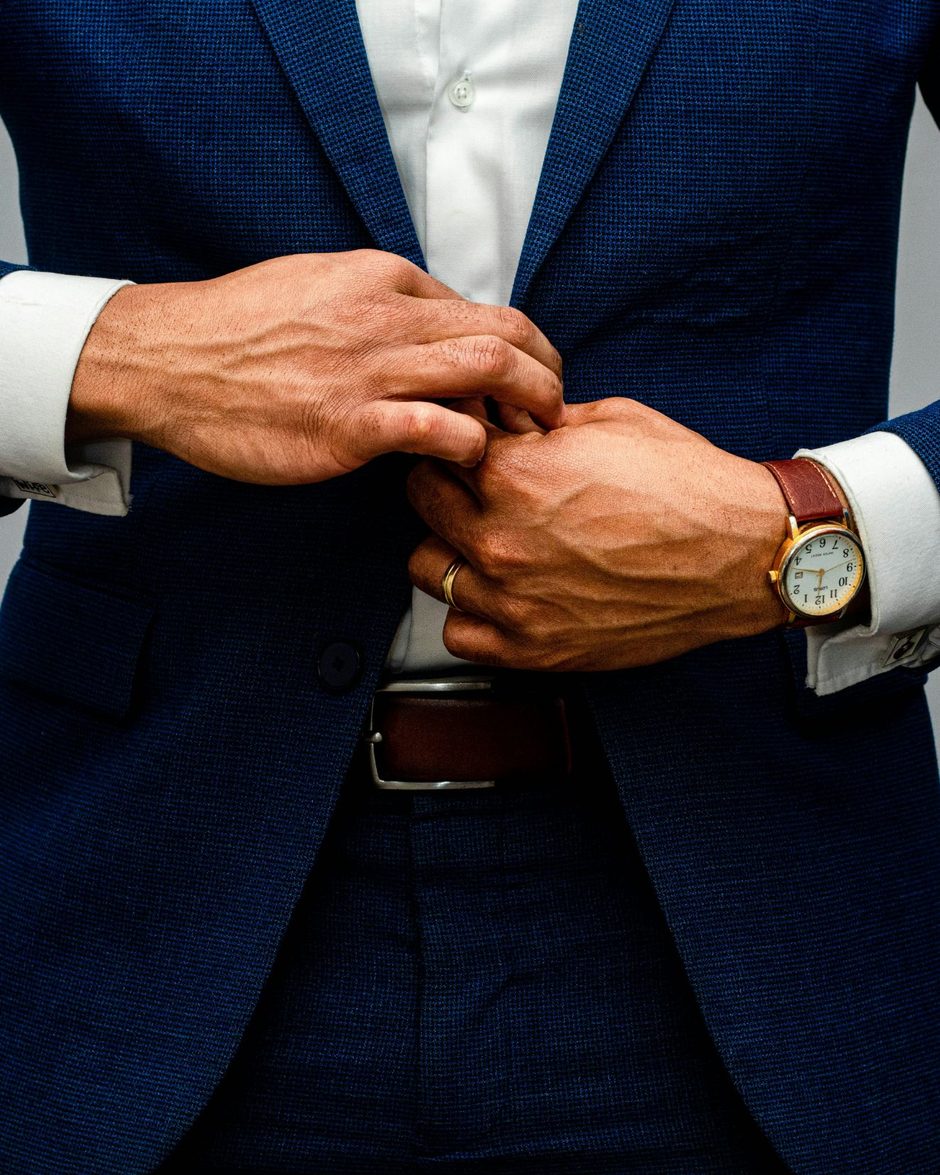 The Franchise OG buttoning a navy suit jacket, gold watch on his wrist
